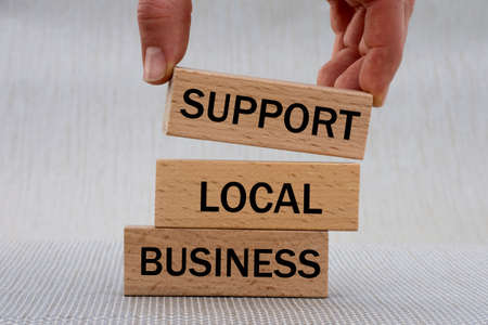 Women's hand folds wooden bars with words SUPPORT, LOCAL, BUSINESS. Business conceptの写真素材