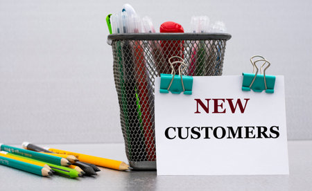 NEW CUSTOMERS - word on a white sheet with clips against the background of cans of pencils. Business...