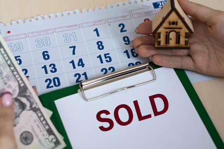SOLD - word in a folder against the background of women's hands with a house and money. Business...