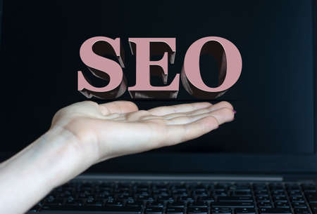 SEO - word on a woman's hand against the background of a laptop. Internet concept