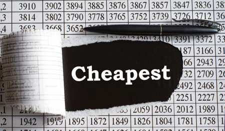 CHEAPEST is the word behind torn office paper with numbers and a black pen. Business and finance conceptの写真素材