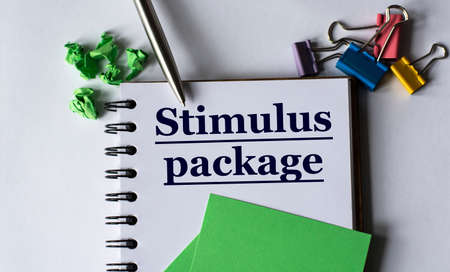 STIMULUS PACKAGE - words in a notebook with stationery clips, pen and green papers. Business concept