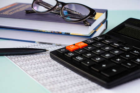 Close-up calculator against the background of the table with numbers, pen, books and glasses. Business conceptの写真素材