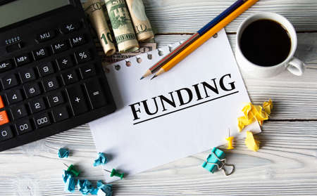 FUNDING - word on a white sheet against the background of a calculator, banknotes, cups of coffee and pencils. Business conceptの写真素材