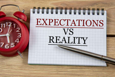 EXPECTATIONS VS REALITY - words in a notebook on a wooden background with a pen and an alarm clock. Business conceptの写真素材