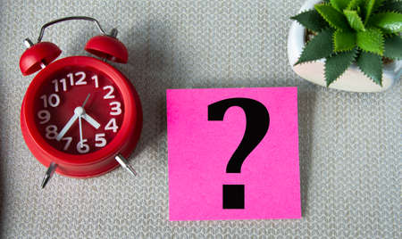 Question mark on note sheet on gray background with alarm clock and cactus