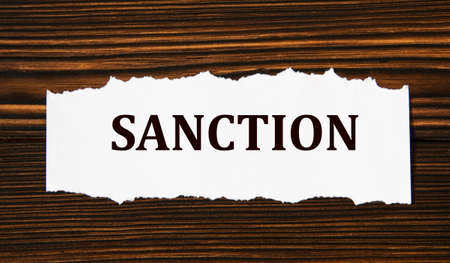 SANCTION - word on a white tattered piece of paper on a wooden background. Info conceptの写真素材