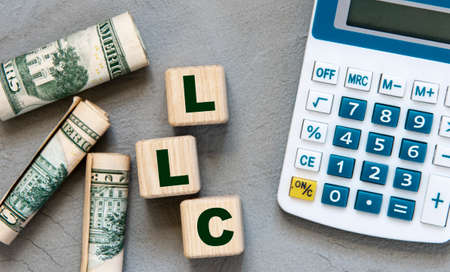 LLC (- Limited Liability Company) acronym on wooden cubes on a gray background with a calculator and...