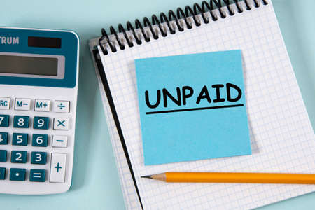 Unpaid - word in a white notebook on a blue piece of paper on the background of a calculator. Business and finance conceptの写真素材
