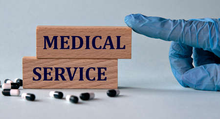 MEDICAL SERVICE - words on wooden blocks on the background of a hand in a medical blue glove and pills. medical conceptの写真素材