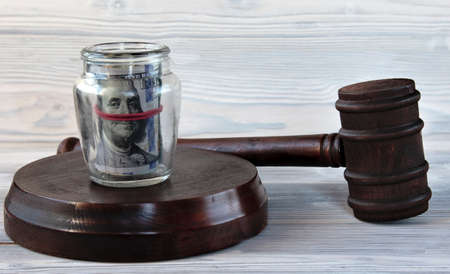 The referee's hammer lies on a light wooden background. A glass jar with dollar bills is on a stand. concept justiceの写真素材