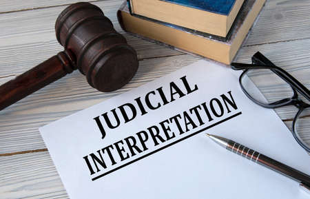 JUDICIAL INTERPRETATION - words on white paper with the background of the judge's hammer, glasses...