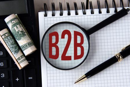 Letters B2B under a magnifying glass on a white notebook against the background of a fragment of a...