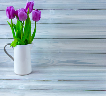 White jug with purple tulips on a wooden light wooden backgroundの写真素材