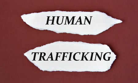 HUMAN TRAFFICKING - words on white torn pieces of paper on a burgundy backgroundの写真素材