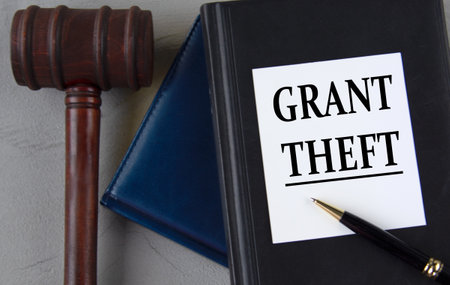 GRANT THEFT - words on a white sheet with leather notebooks, a judge's hammer and a penの写真素材