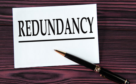 REDUNDANCY - word on a white sheet on a brown wooden background with a pen. info conceptの写真素材