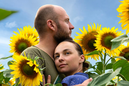 Couple enjoying summer time in a field of sunflowers. And green forest in the backgroundの写真素材