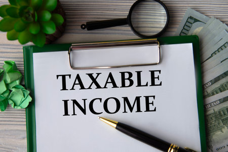 TAXABLE INCOME - words on a white sheet against the background of banknotes, magnifying glass and cactusの写真素材