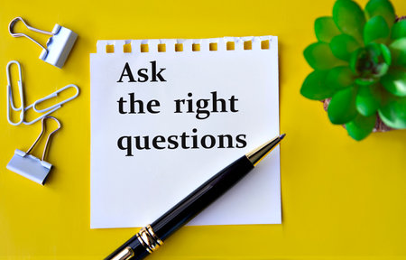 ASK THE RIGHT QUESTIONS - words on a white sheet with a pen, stationery clips and a cactus. Info conceptの写真素材