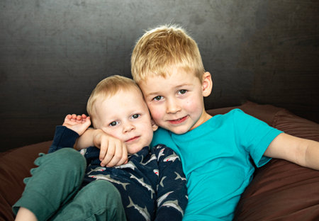 Portrait of two boys sitting in an embrace in a roomの写真素材