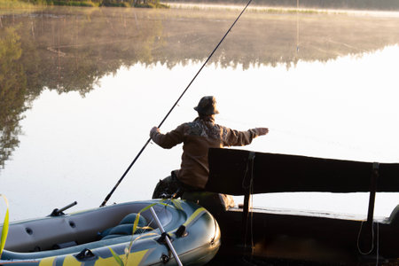 A man sits on a wooden bench and catches a fish with a fishing rod. There is a beautiful forest lake...
