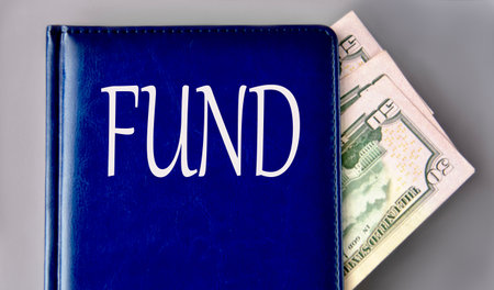 FUND - word on a blue book on a gray background with banknotes. Business conceptの写真素材