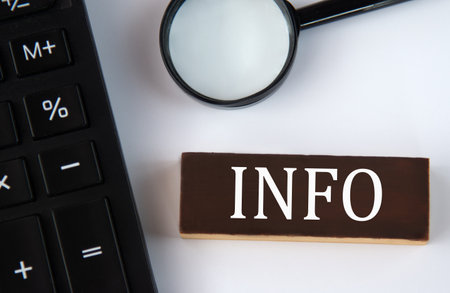 INFO - word on a brown wooden block with a calculator and magnifying glass in the background. Business conceptの写真素材