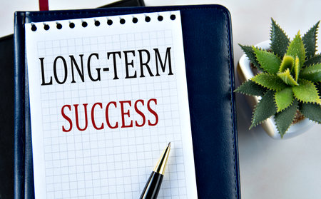 LONG-TERM SUCCESS - words on white sheet on light background with notebook and cactusの写真素材