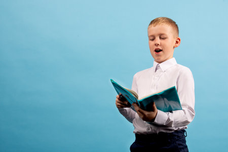 Little schoolboy with a notebook on a blue background. Studio shot. Education conceptの写真素材
