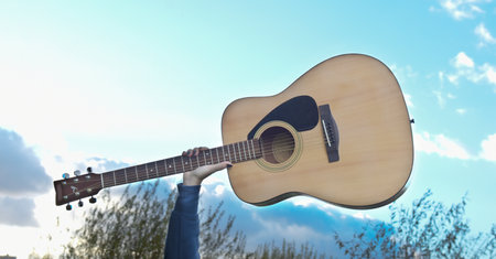 Close-up guitar in hand against blue sky background