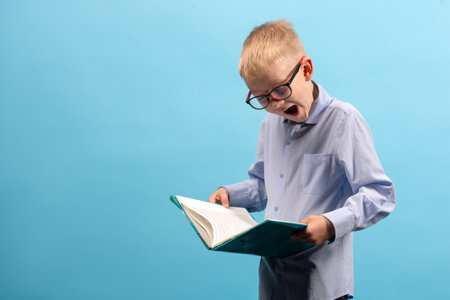 An 8-9-year-old boy looks at a notebook in surprise. A studio shot. The concept of educationの写真素材