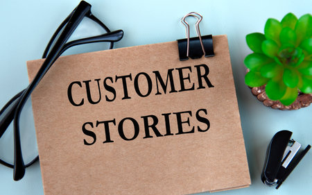 CUSTOMER STORIES - words on brown paper on a light background with glasses, cactus and staplerの写真素材