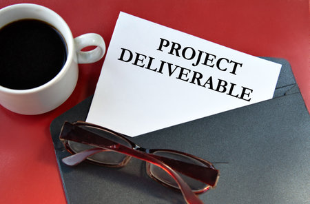 PROJECT DELIVERABLE - words on white paper lying on a black envelope on a red backgroundの写真素材