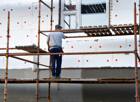 A worker lays wall tiles on the wall of a house using scaffoldingの写真素材