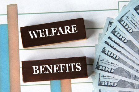 WELFARE BENEFITS - words on brown wooden blocks on the background of a graph and banknotesの写真素材