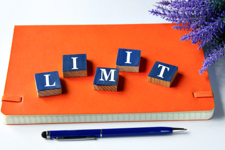 LIMIT - a word written on wooden cubes on an orange notepad with a pen lying nearby