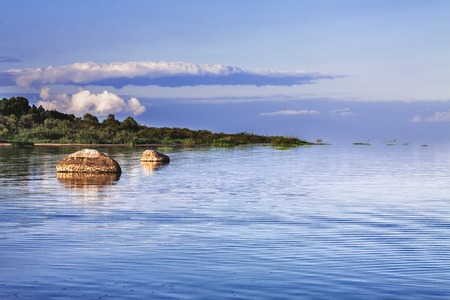 A large stone near the shore of the lake against the background of beautiful clouds.の写真素材