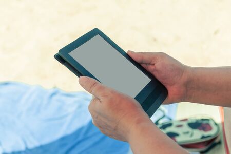 Woman on the beach reads an e-bookの写真素材