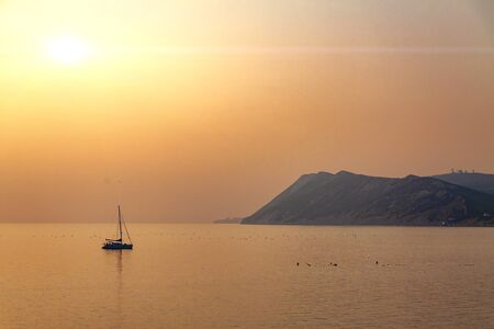 Sunset at sea, against the backdrop of boats and mountains.
