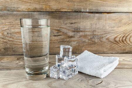 Glass with foda, next to ice cubes and a towel layer on a wooden backgroundの写真素材