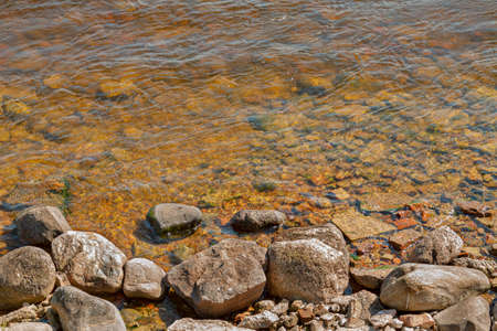Small stones on the shore of a lake with clean water.の写真素材
