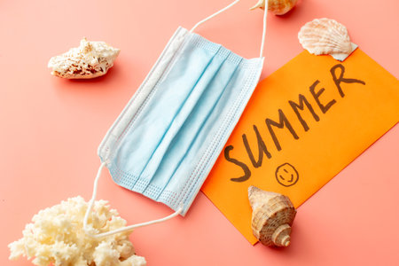 background image with summer vacation concept during quarantine: medical mask, seashells on pink...