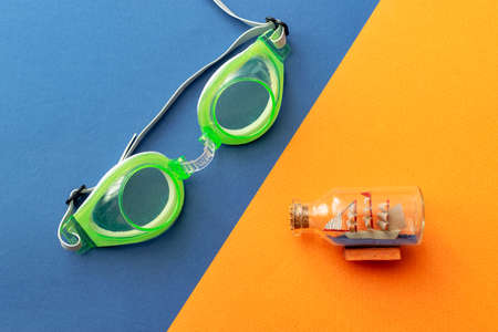 green swimming goggles with a ship in a bottle on an orange and blue backgroundの写真素材