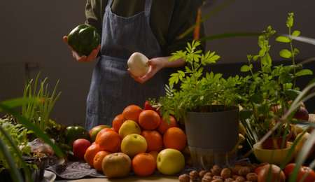 A woman is holding a pepper and a bunch of oranges. The oranges are piled up on a table