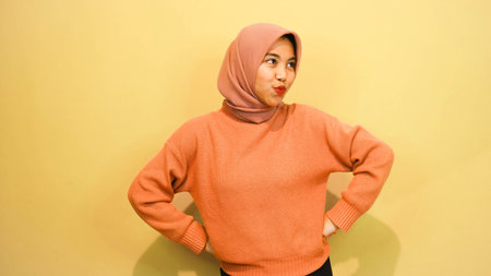 Portrait of young beautiful asian muslim woman wearing hijab isolated on orange background