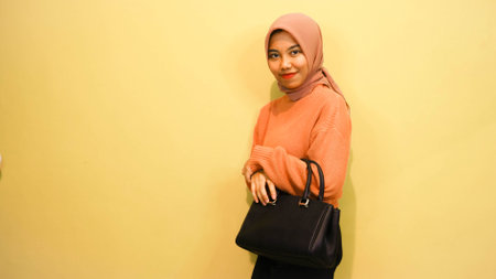Happy Asian girl woman holding black bag standing over orange background studio shot, Close up...