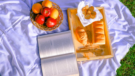 Basket of fresh fruits, bread, croissants and a book on the grass. Picnic concept