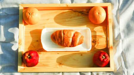 Croissant and fruit in wooden tray on white napkin. Top view