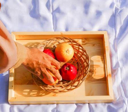 Man's hand holding a basket with fresh fruits on a wooden trayの写真素材